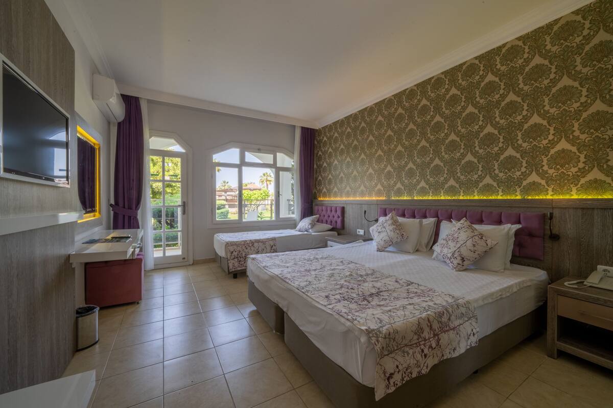 Une chambre d’hôtel avec deux lits, une télévision, un bureau et une fenêtre donnant sur un paysage verdoyant.