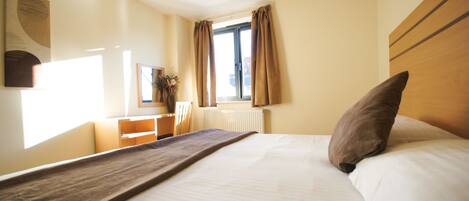 Habitación de hotel con cama, escritorio, silla, ventana con cortinas y radiador.