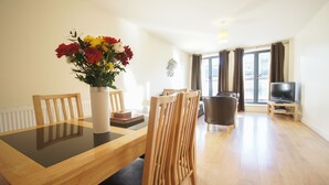 A modern living room with a dining table, chairs, a TV, and a vase of flowers. - Crompton Court (London)