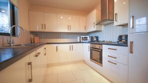 A modern kitchen with white cabinets, stainless steel appliances, and a tiled backsplash. - Crompton Court (London)
