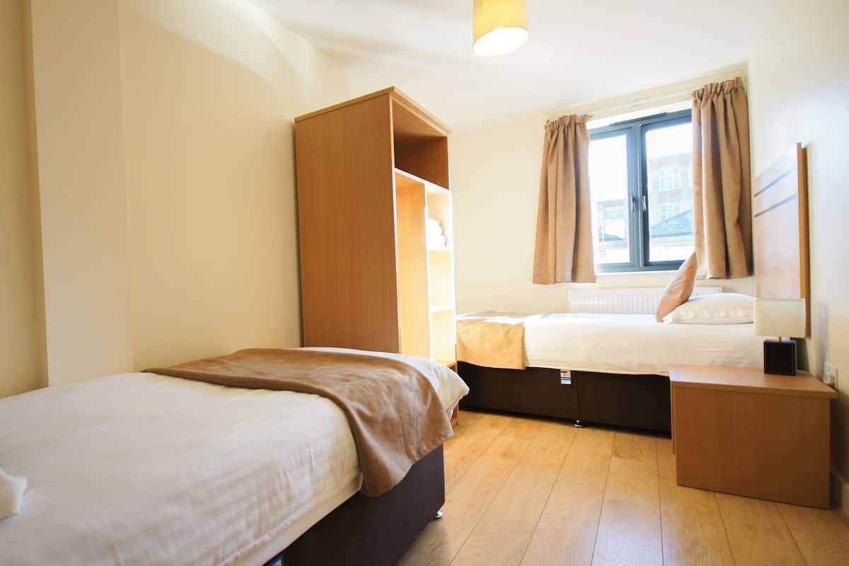 A bedroom with two beds, a wardrobe, a bedside table, and a window with curtains.