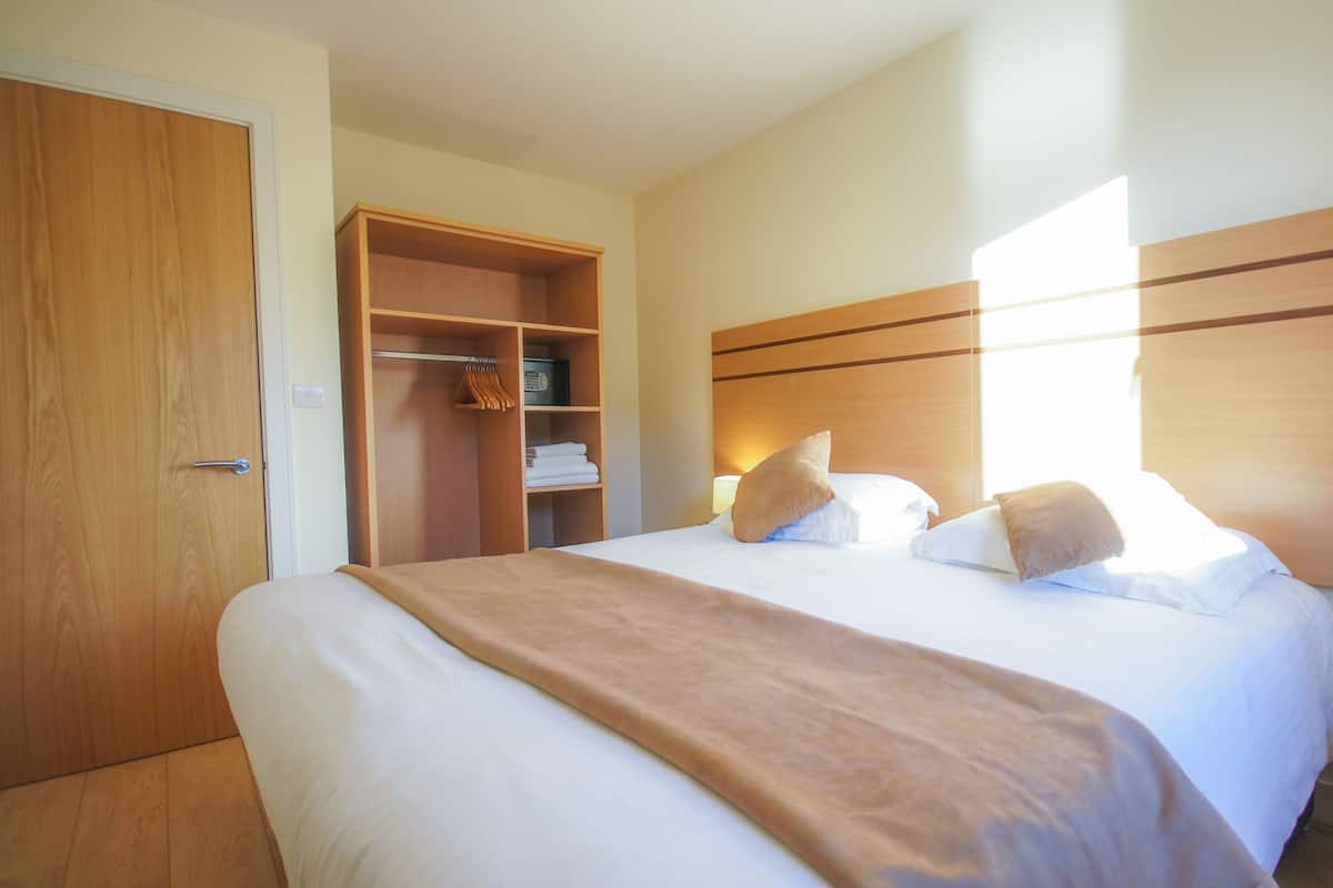 A hotel room with a large bed, a wooden wardrobe, and a bedside table with a lamp.