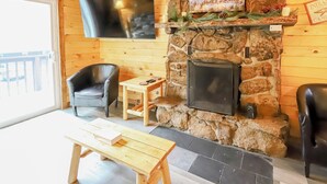 A cozy room with a stone fireplace, a television mounted above it, two leather chairs, and a wooden table. - Nicky's Resort (Estes Park)