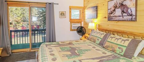 A bedroom with a large bed, a balcony with a view, a fan, and a painting of animals.