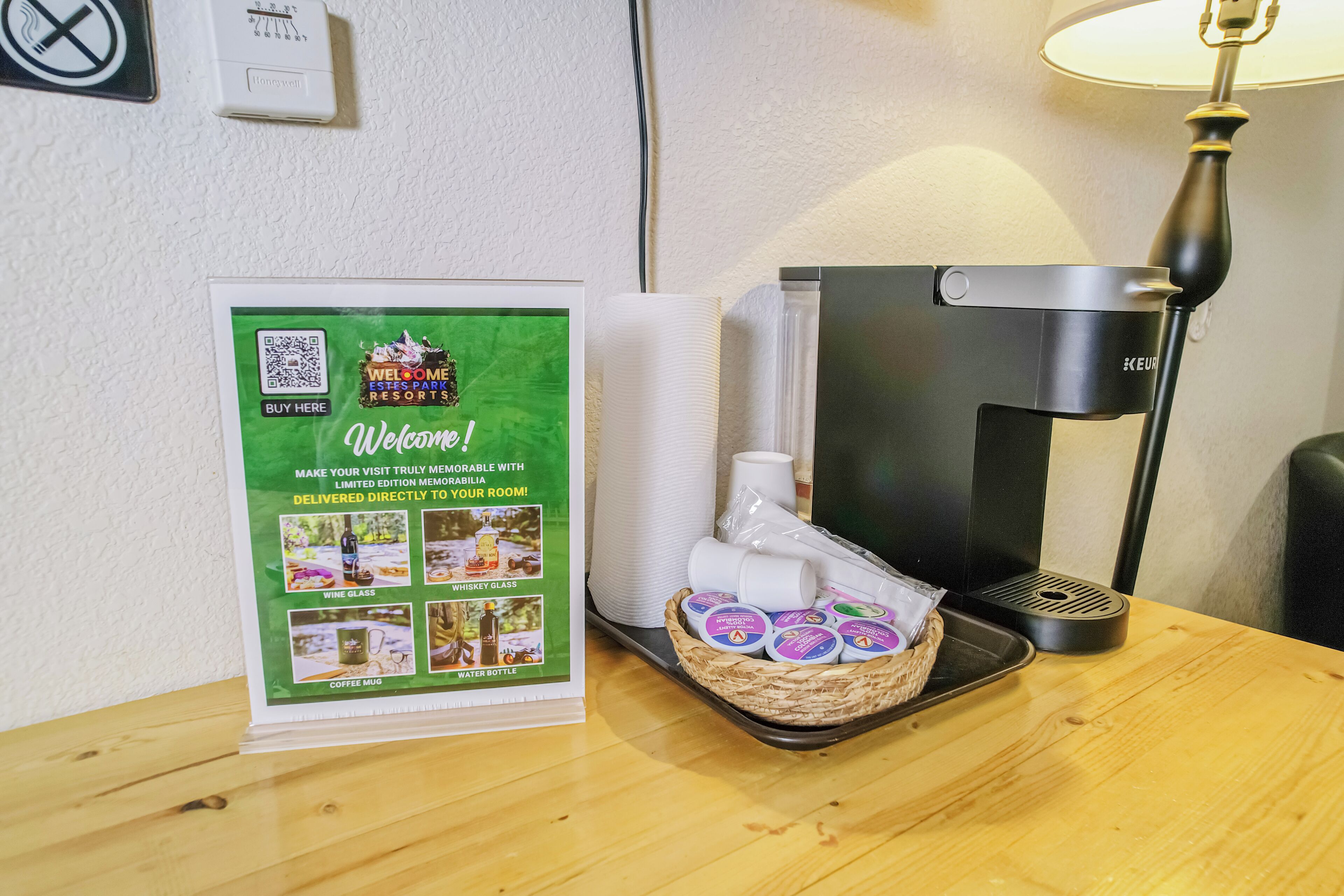 A welcome sign with a QR code, a tray with disposable cups, a water bottle, and a coffee machine on a wooden table.