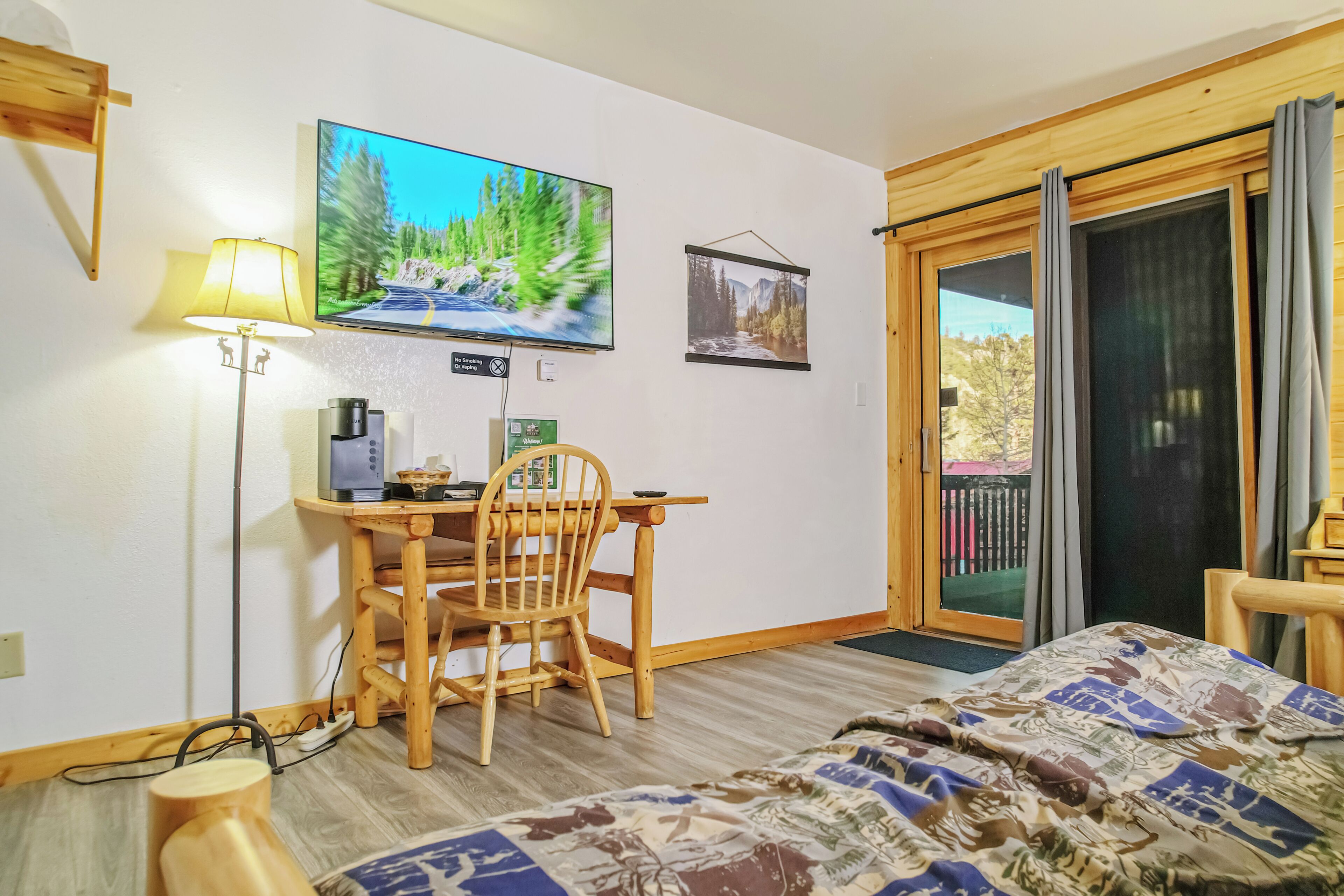 Una habitación con una cama, un escritorio con una silla, un televisor montado en la pared y un ventanal corredero que da a un espacio exterior.