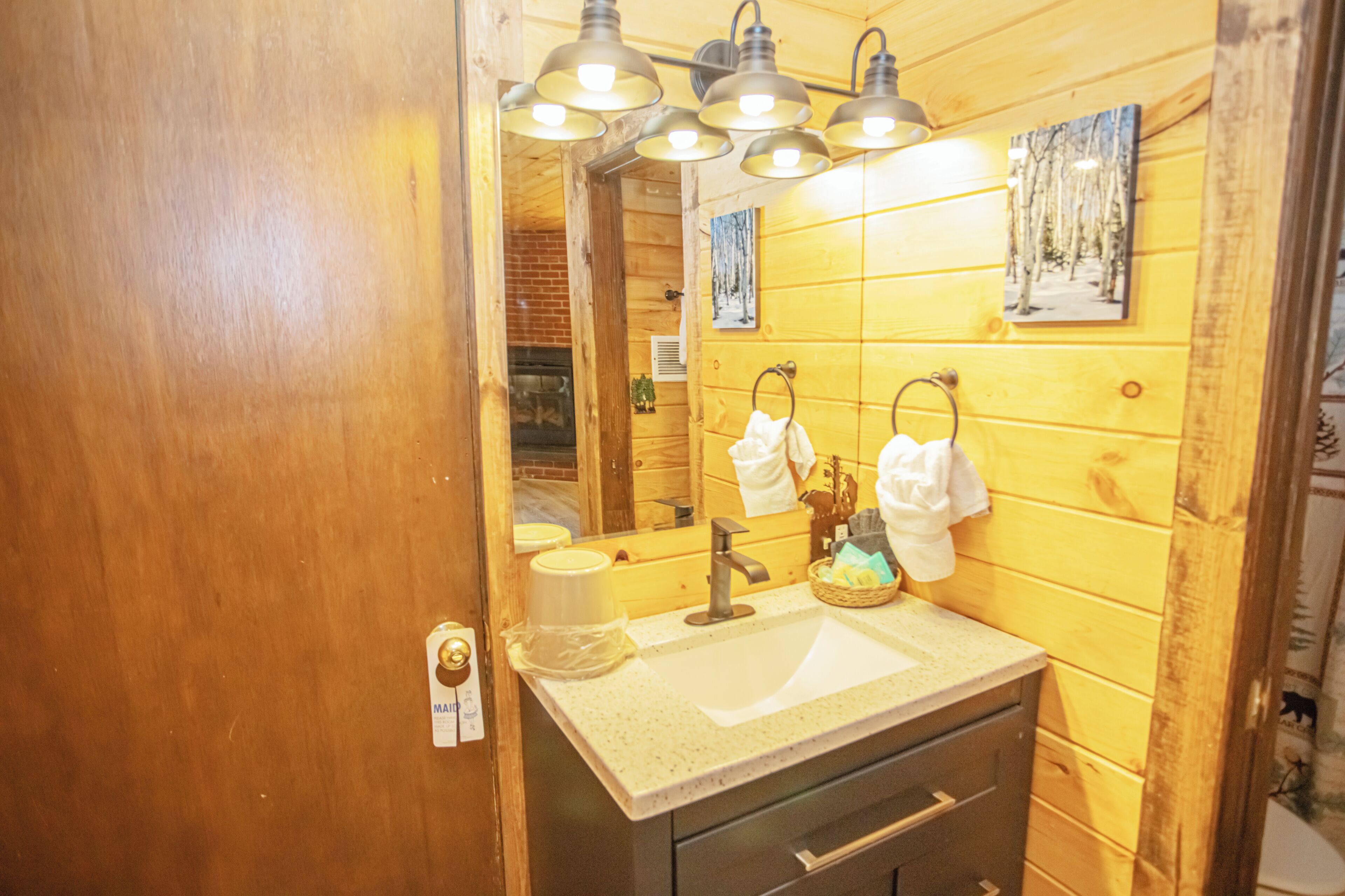 A wooden cabin-style bathroom with a sink, mirror, towel rack, and a small basket.
