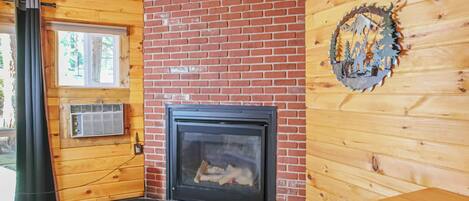 Interior de una cabaña de madera con chimenea, una ventana y una puerta.