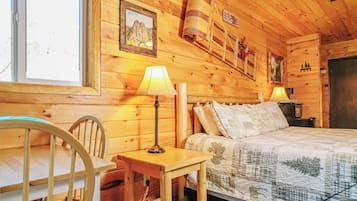 Una habitación de cabaña de madera con una cama, dos lámparas, una silla y una ventana.