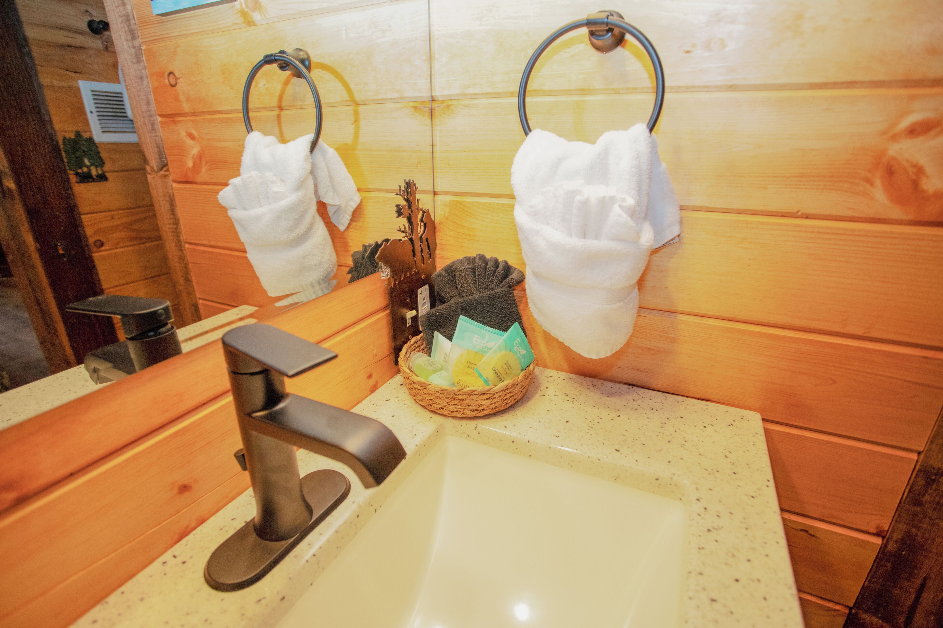 Un baño con paneles de madera, un lavabo con grifo moderno y dos toallas colgadas en aros.