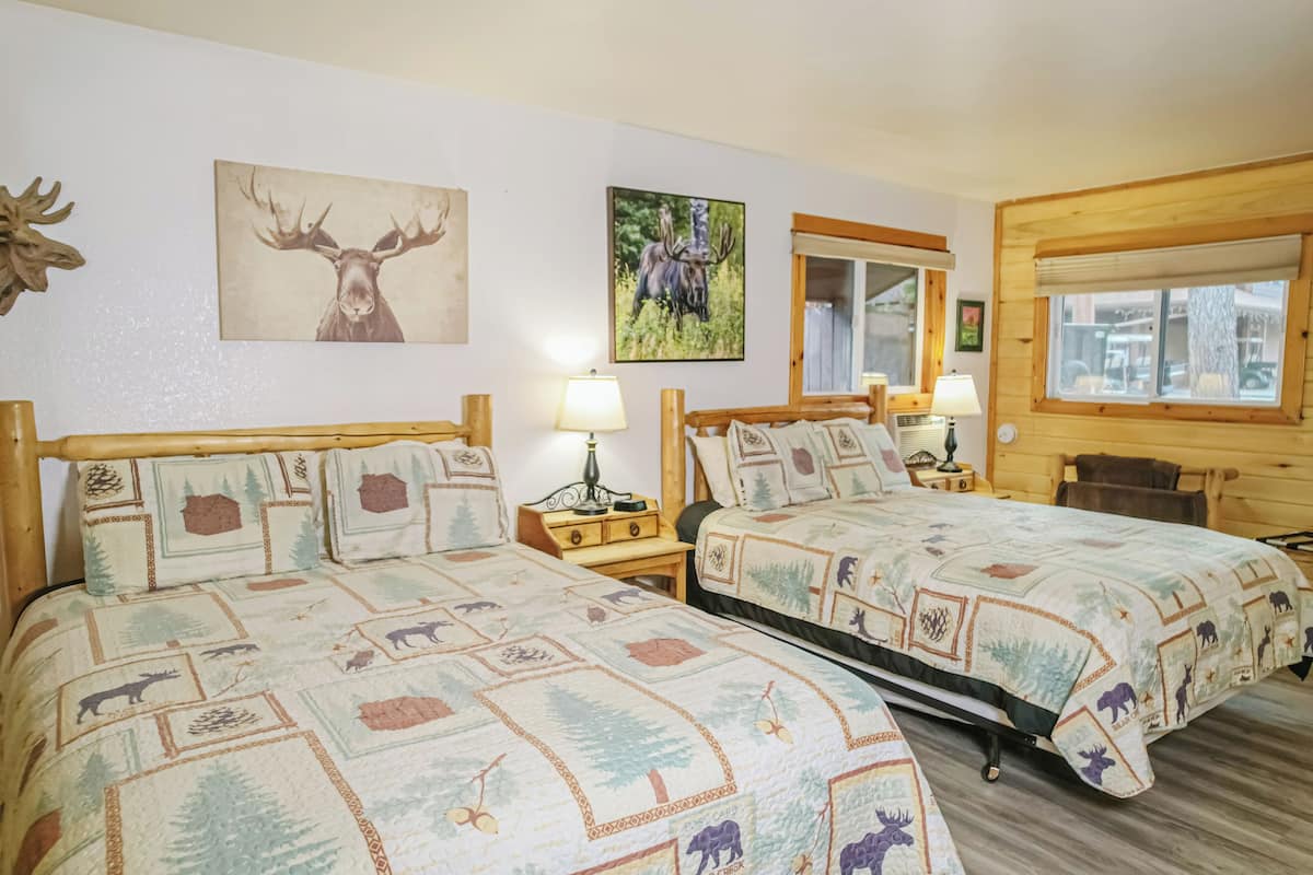 Two double beds with forest-themed bedding, wooden headboards, bedside tables with lamps, and wall-mounted artwork.