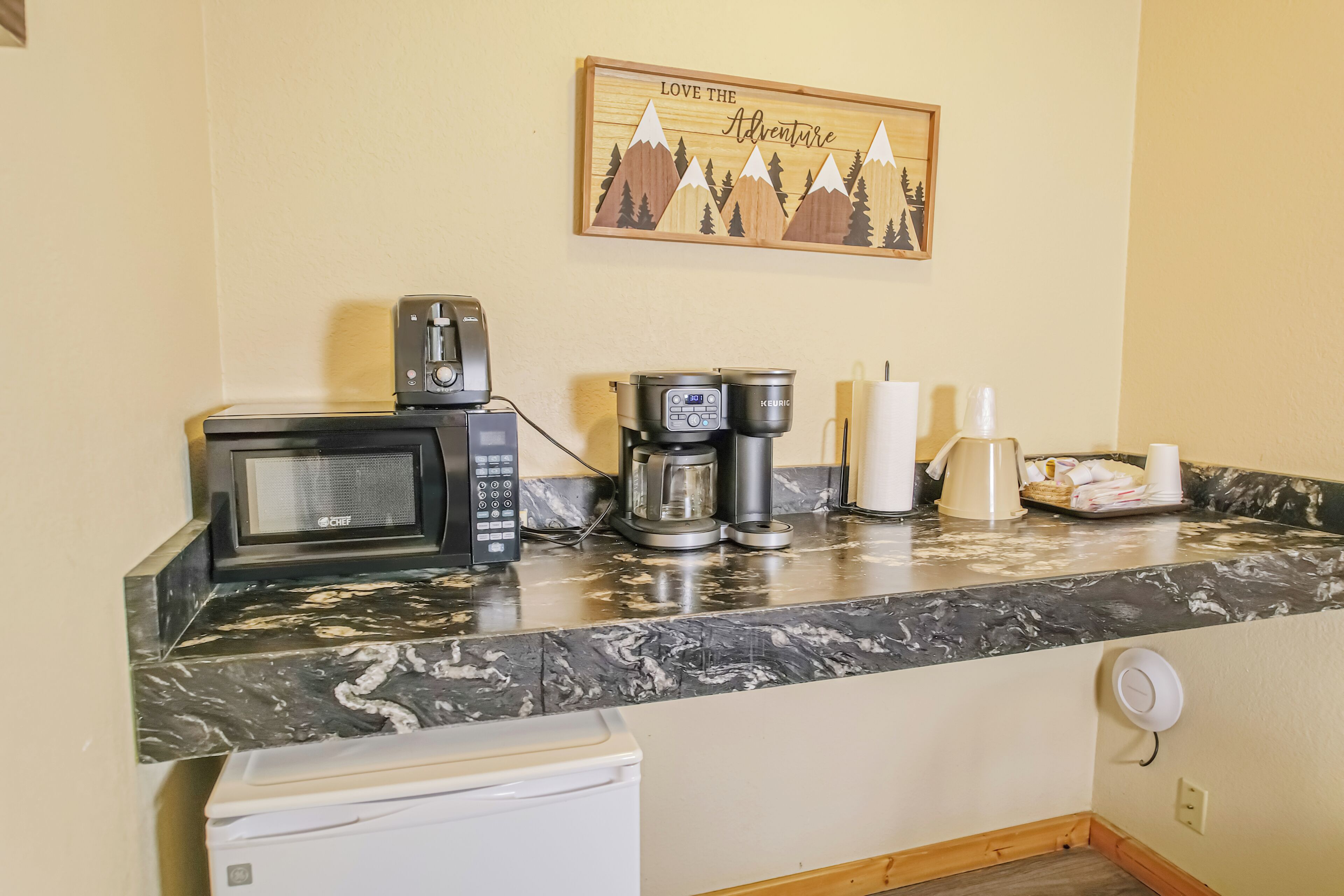 A kitchen with a microwave, coffee maker, and a coffee pot on the counter.