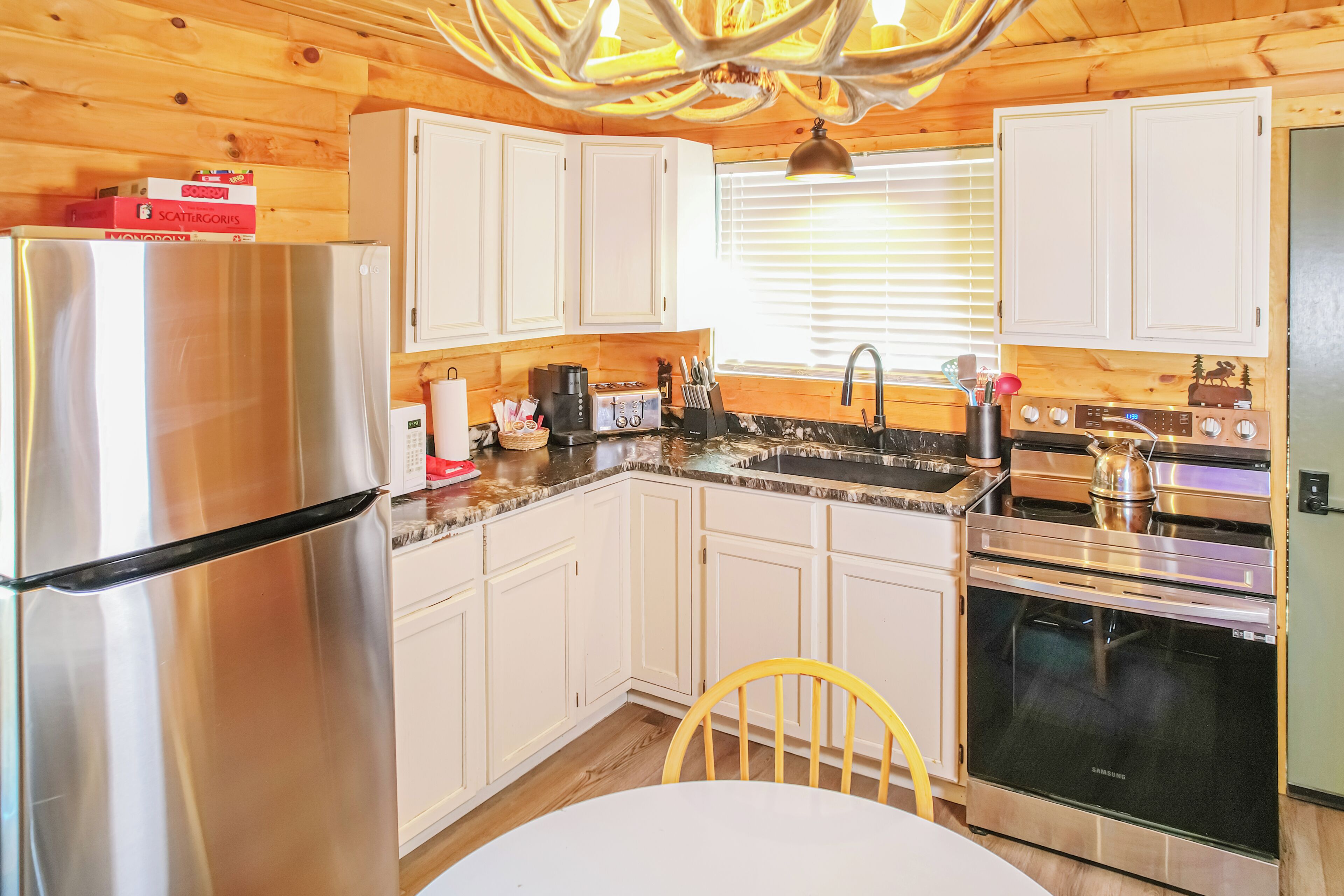 A kitchen with white cabinets, stainless steel appliances, a granite countertop, and a dining table with a chair.
