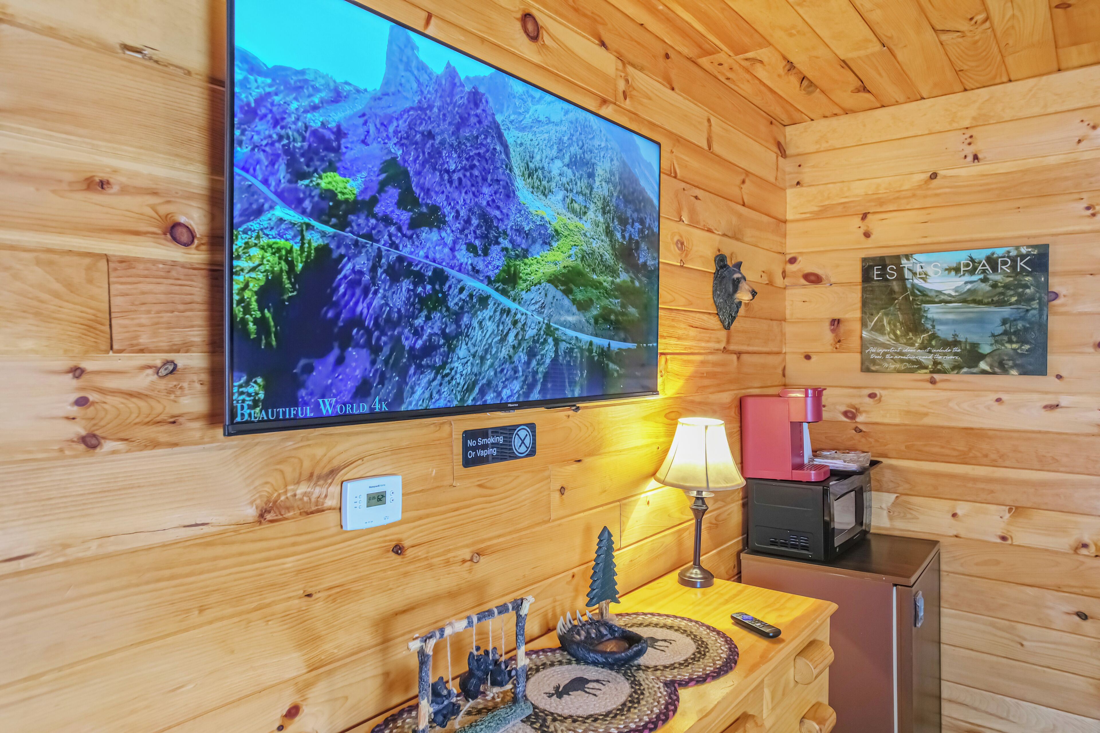 Interieur van een houten hutje met een televisie waarop een natuurscène te zien is, een rookvrij bord, een lamp, een koffiezetapparaat en een kleine koelkast.