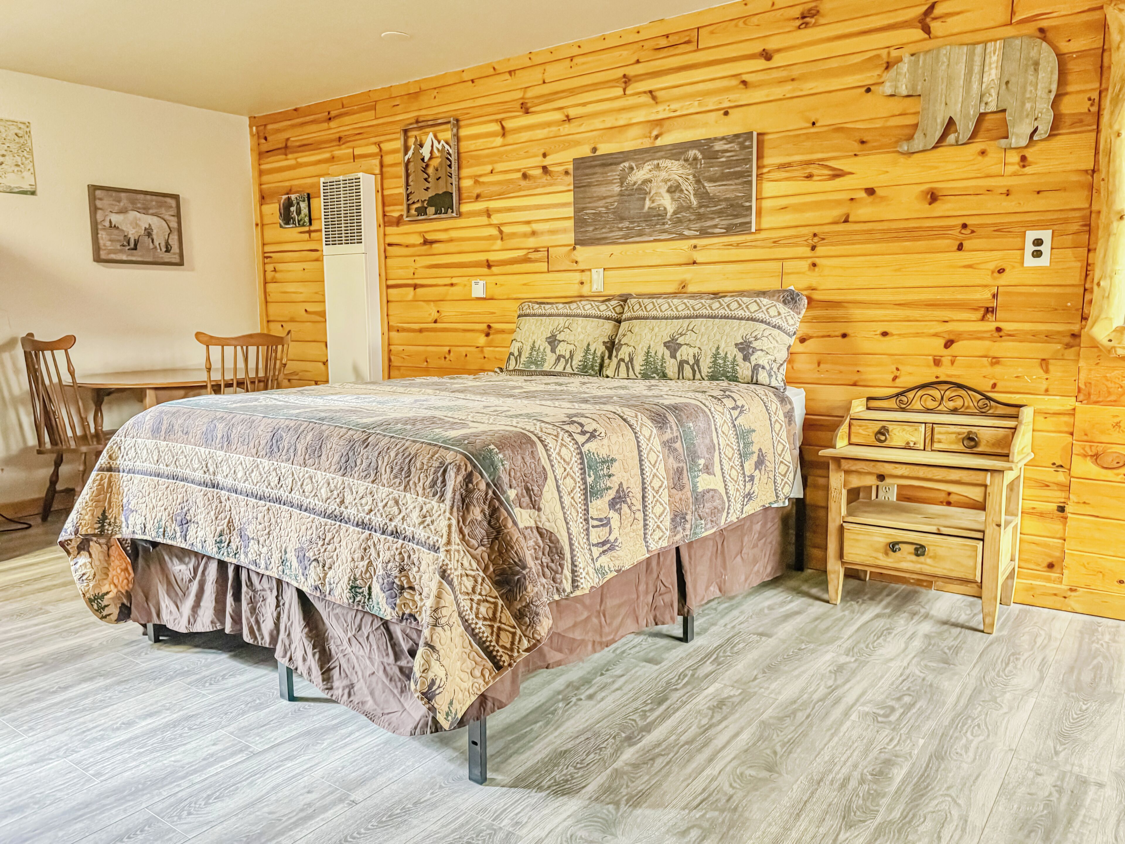 A wooden-paneled room with a bed, a nightstand, a chair, and a wall-mounted heater.