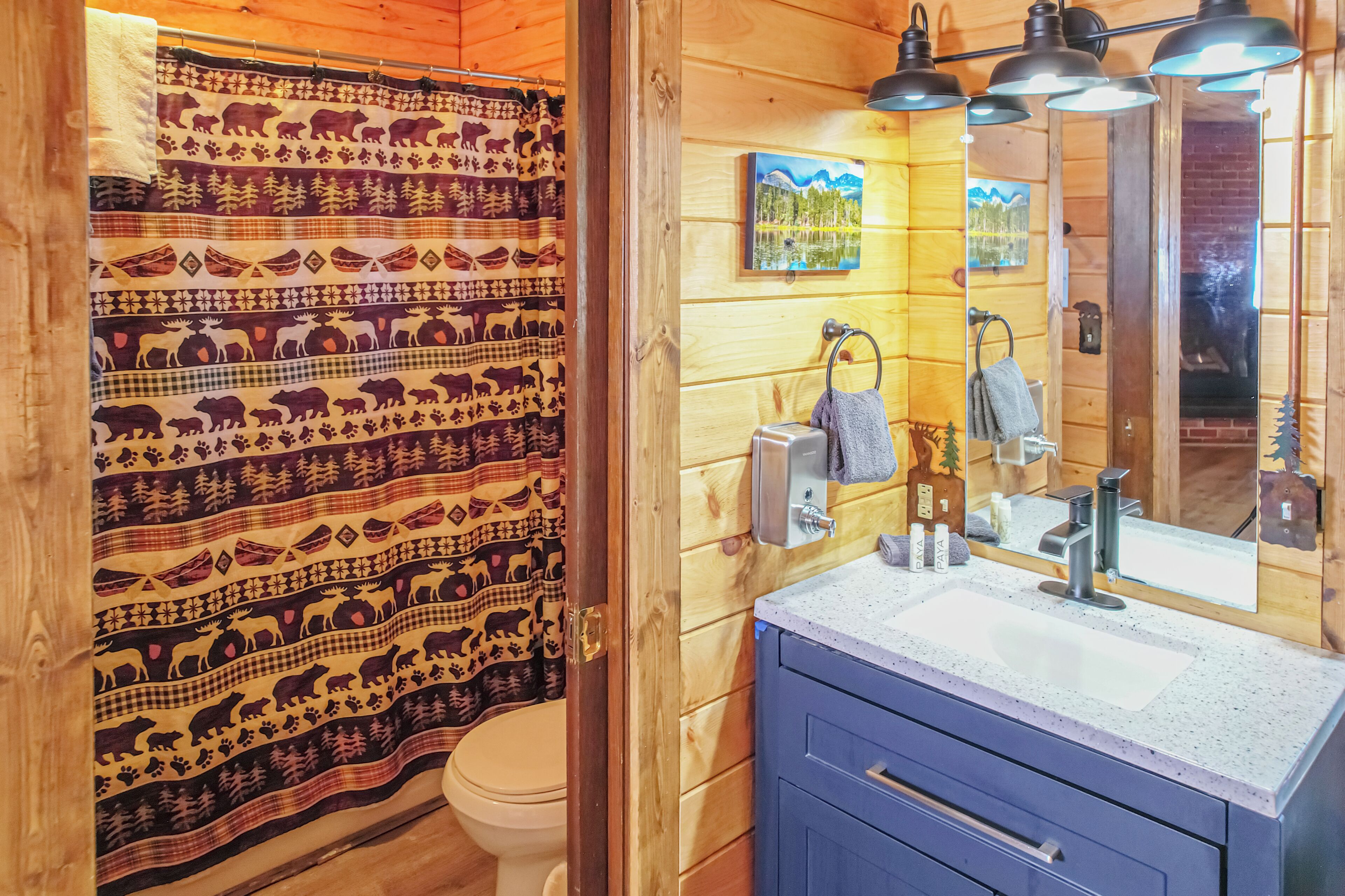 A wooden cabin bathroom with a patterned shower curtain, a sink with a mirror, and a towel rack.