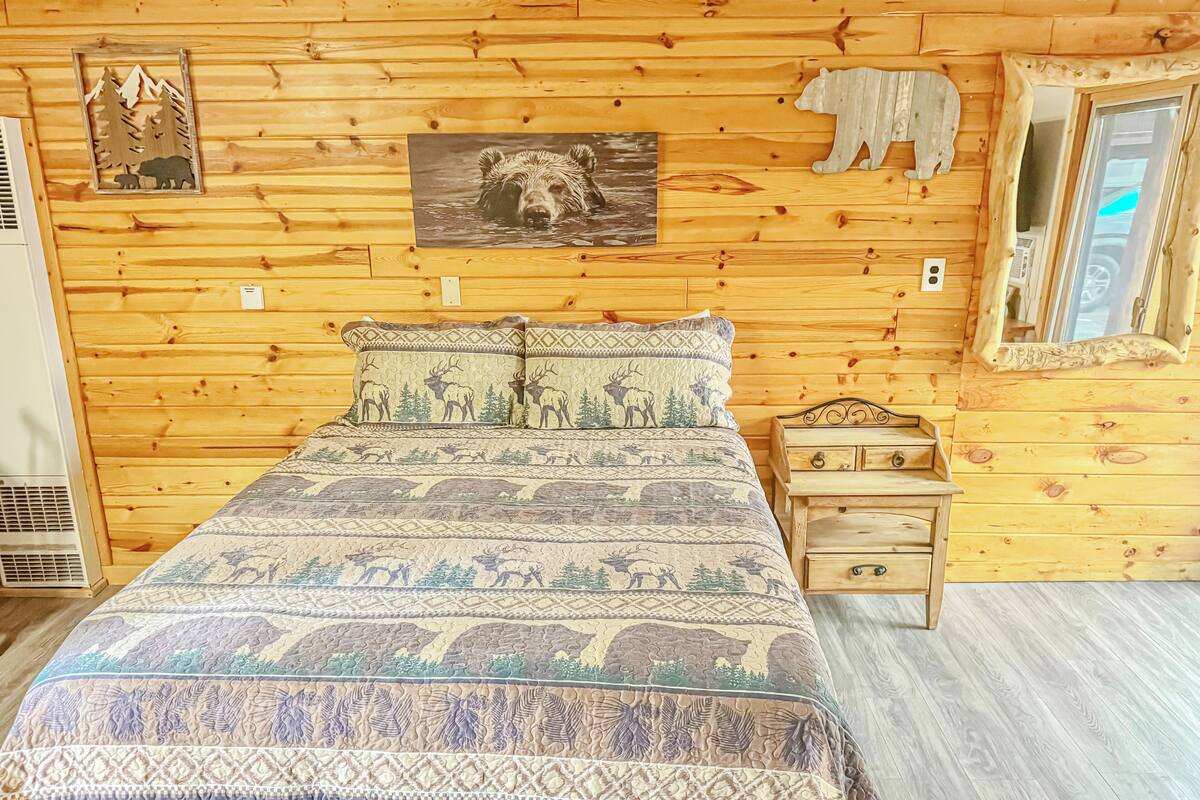 A wooden cabin room with a bed, a nightstand, a mirror, and wall decorations including animal prints.