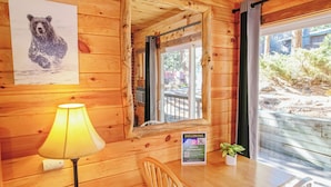 A wooden cabin interior with a table, chairs, a lamp, a mirror, a poster of a bear, and a sign offering a free stay. - Nicky's Resort (Estes Park)