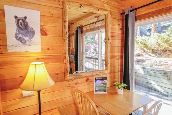 A wooden cabin interior with a table, chairs, a lamp, a mirror, a poster of a bear, and a sign offering a free stay.