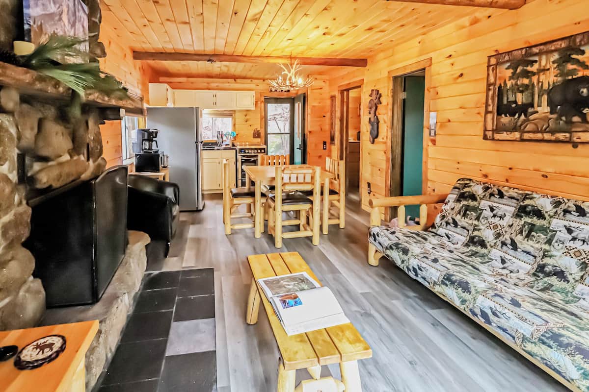 A wooden cabin interior with a stone fireplace, a dining area, and a sofa.