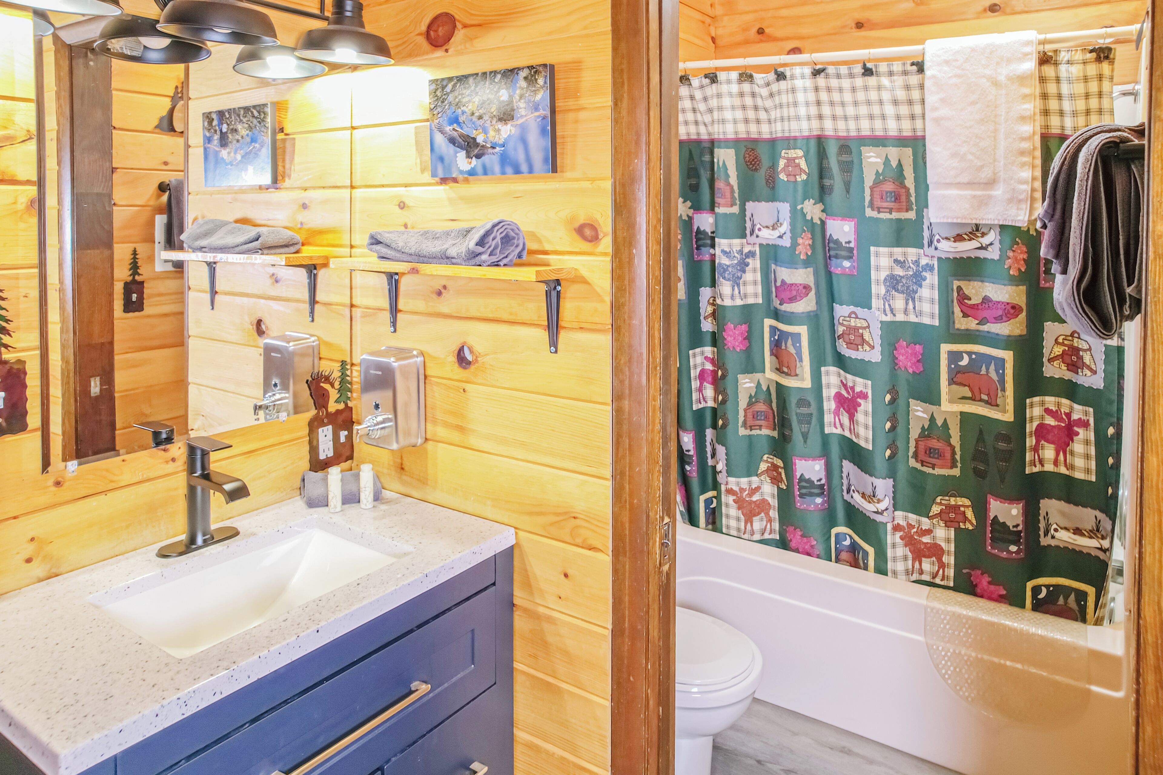 Ein Badezimmer einer Holzhütte mit Waschbecken, Spiegel, Handtuchhalter und einer Duschvorhang mit Muster.