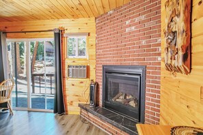 A wooden interior with a fireplace, a sliding glass door to a deck, and a brick wall. - Nicky's Resort (Estes Park)