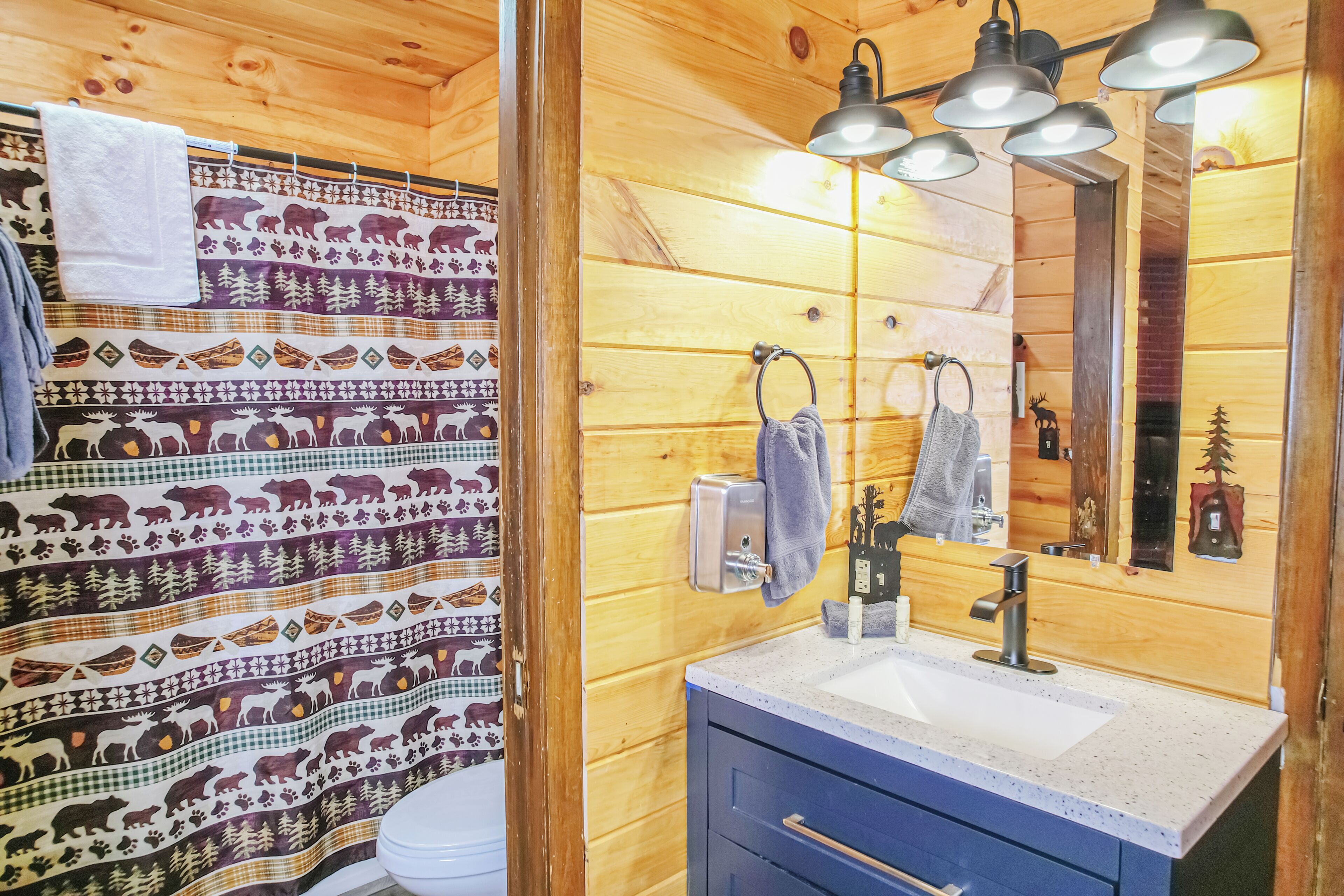 Une salle de bain rustique, avec des murs en bois, un rideau de douche à motifs, un lavabo avec un miroir et un porte-serviettes.