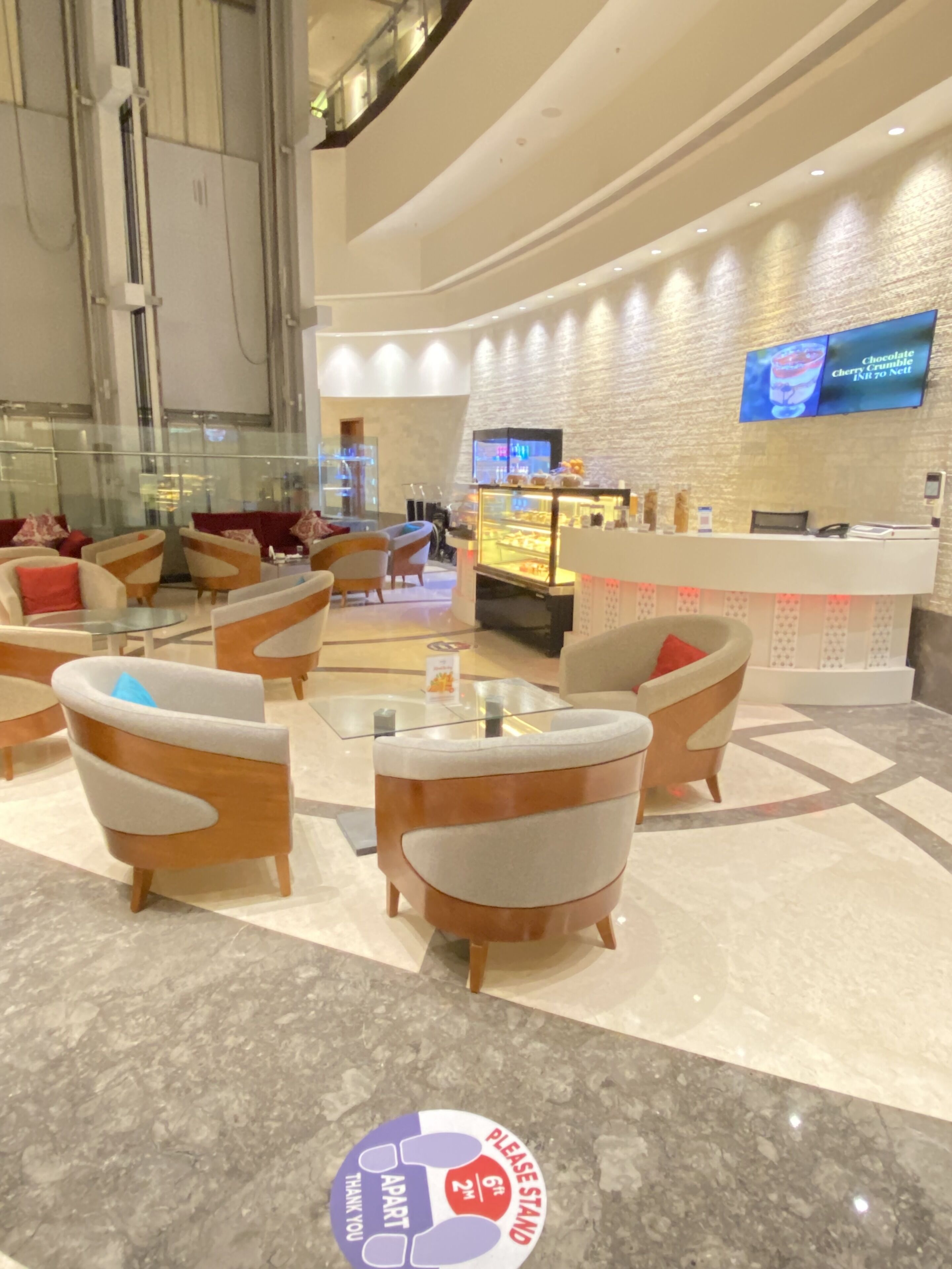 A modern lobby with comfortable seating, a reception desk, and a digital screen displaying a beverage advertisement.