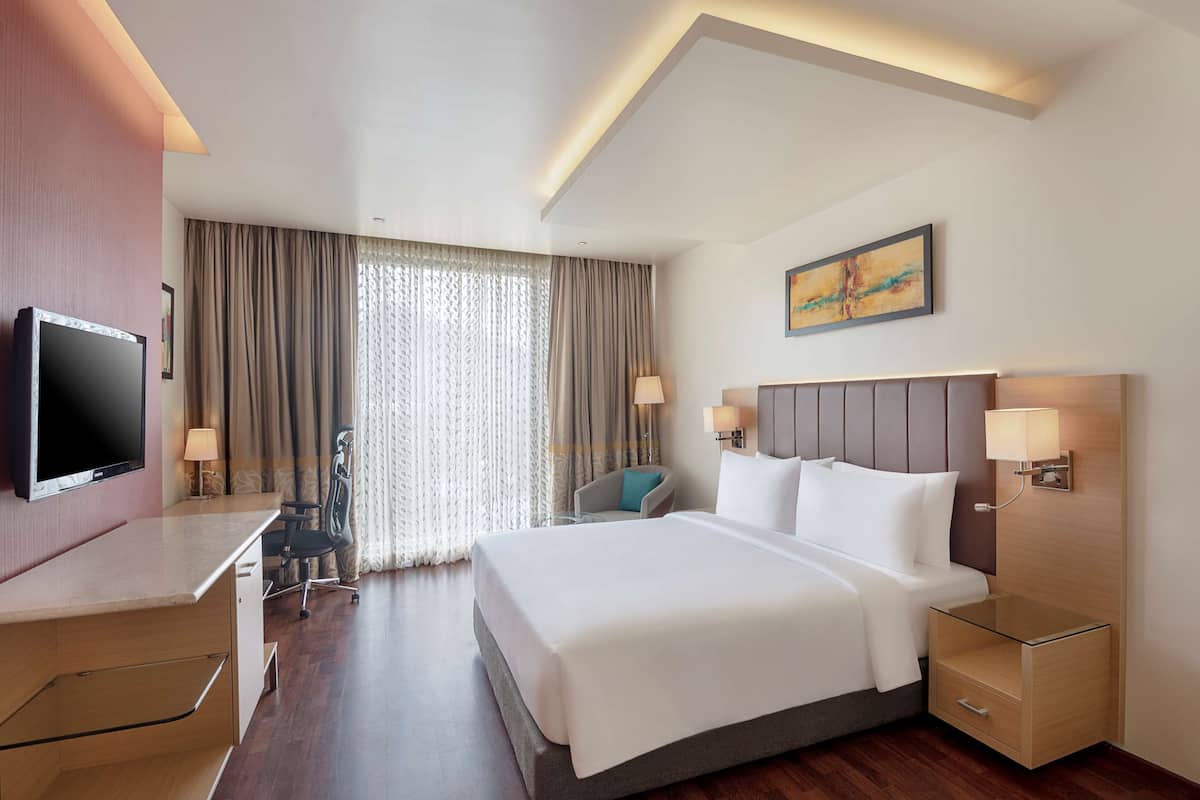 A hotel room with a bed, bedside tables, a desk, a chair, a TV, and a window with curtains.