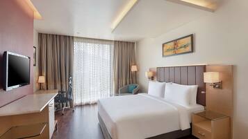 Habitación de hotel con cama, mesitas de noche, escritorio, silla, televisión y ventana con cortinas.