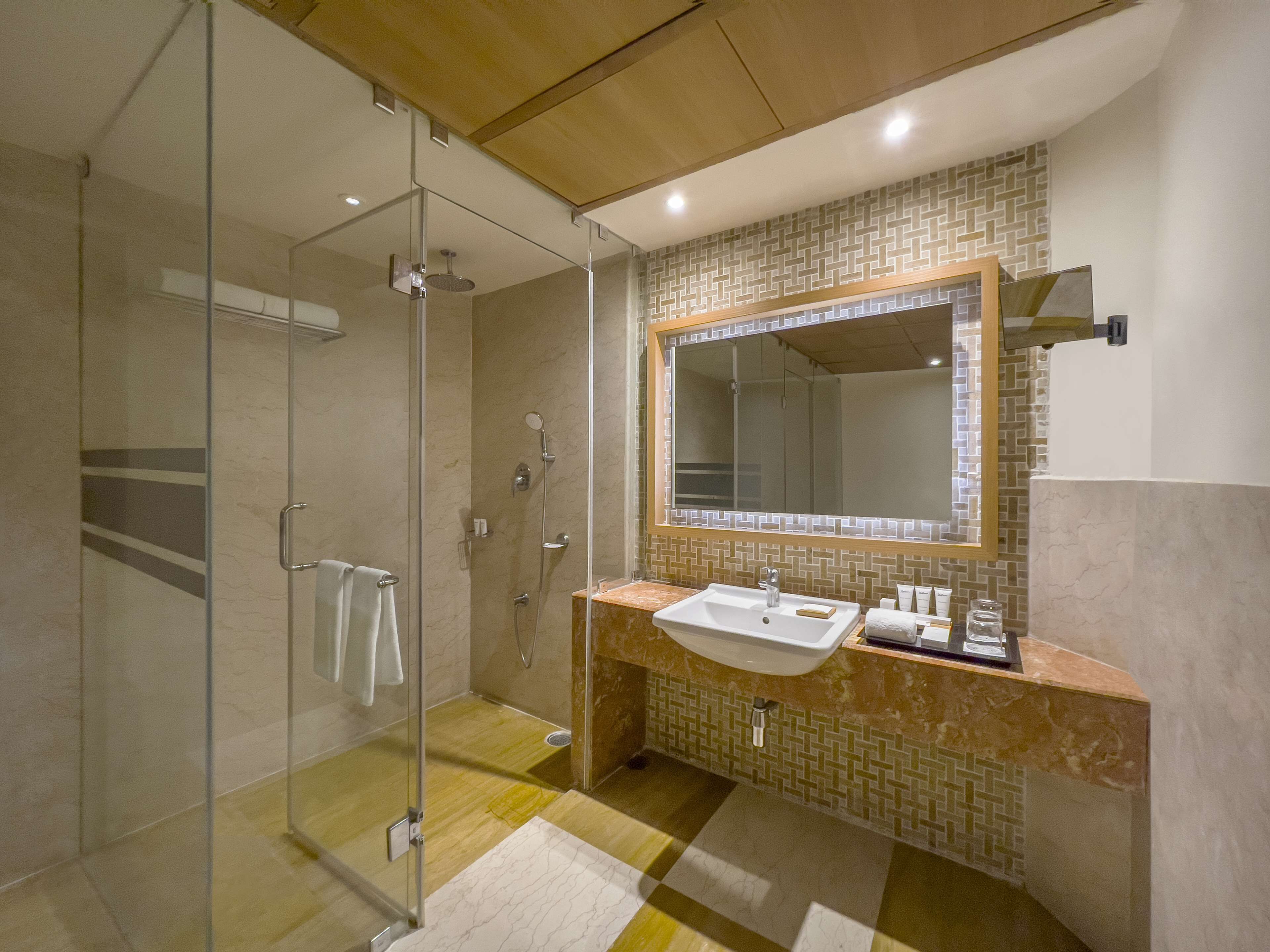 A modern bathroom with a glass-enclosed shower, a large mirror, and a marble-tiled vanity.