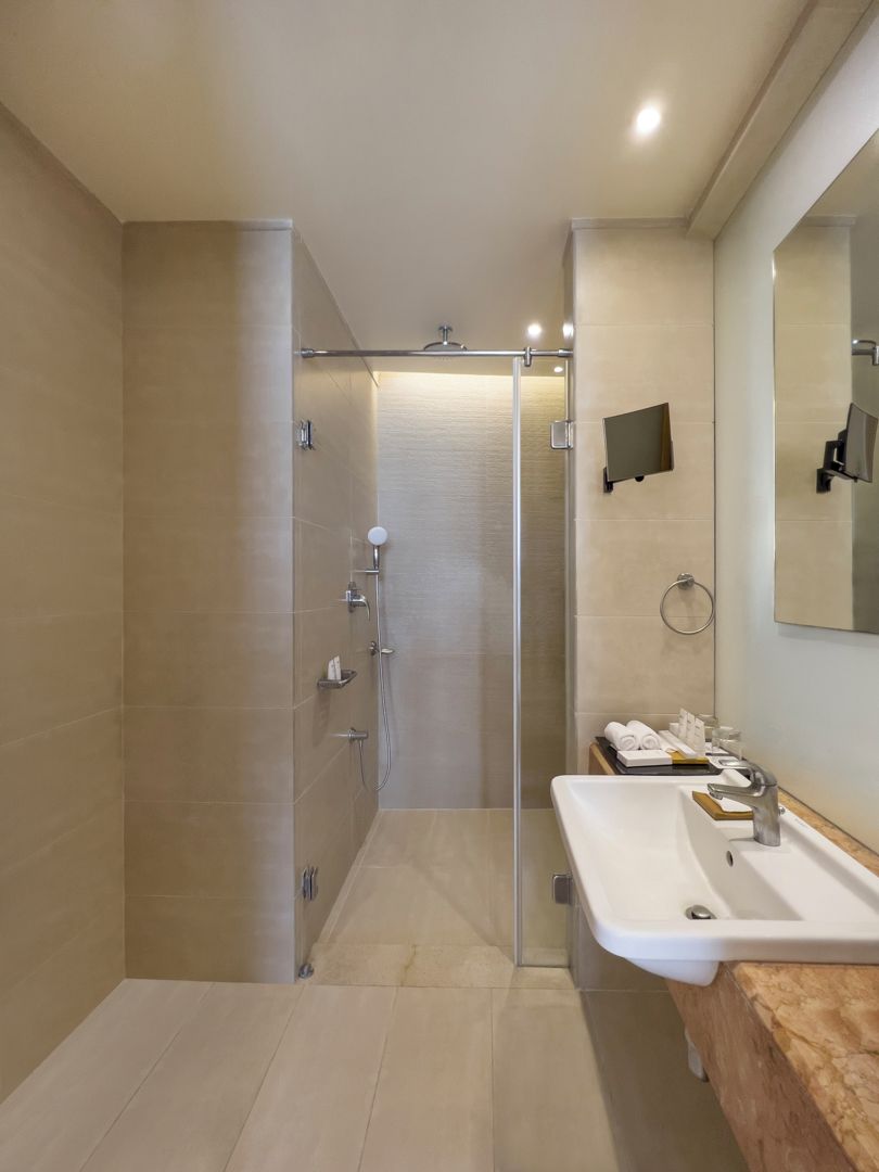 Un baño moderno con ducha envuelta en vidrio, lavamanos con espejo y un perchero para toallas.