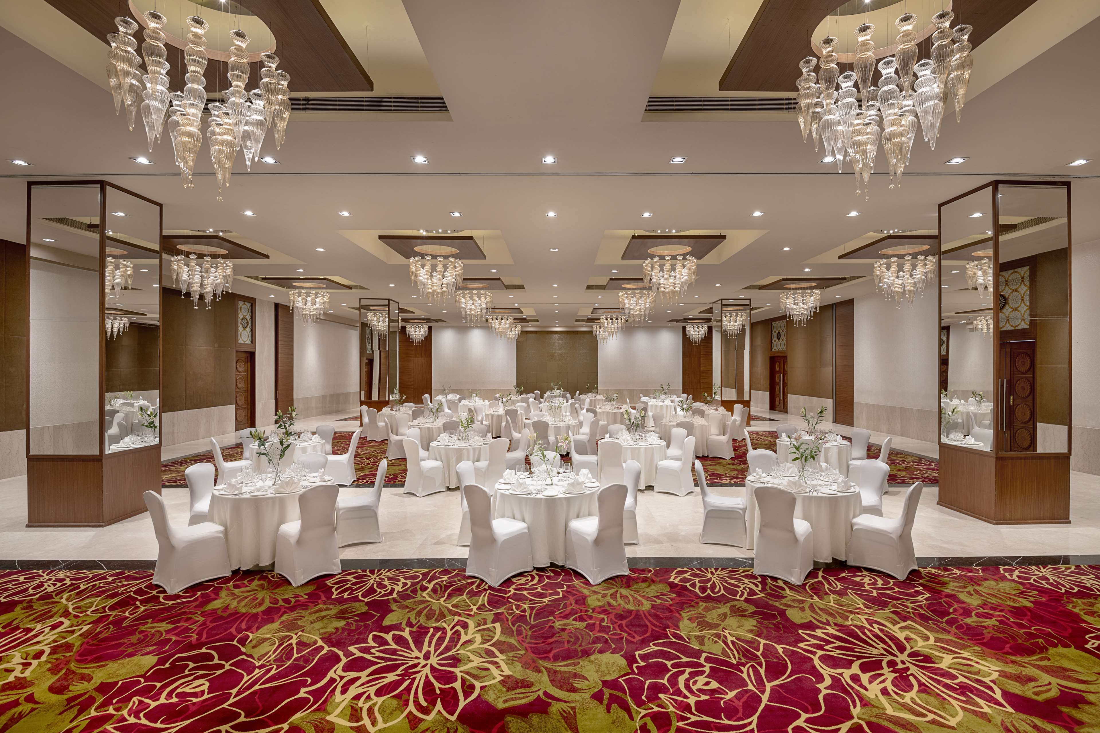 Une vaste salle de banquet avec des tables rondes disposées pour les événements, des lustres et une moquette rouge.