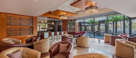 Un hall amplio con sofás de cuero, una zona de bar y ventanas grandes con vistas a palmeras.