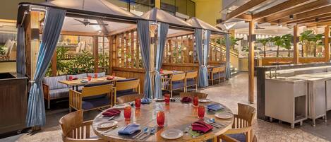 Un restaurant avec des tables rondes, des rideaux bleus et des chaises en bois.