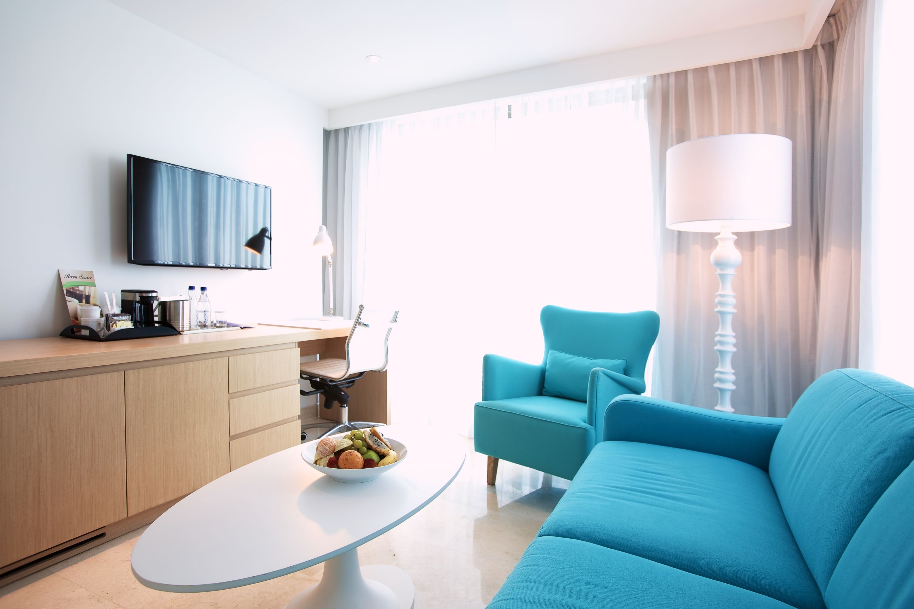 Une chambre d’hôtel moderne équipée d’un canapé, d’une table à manger, d’un téléviseur fixé au mur et d’une fenêtre avec des rideaux.