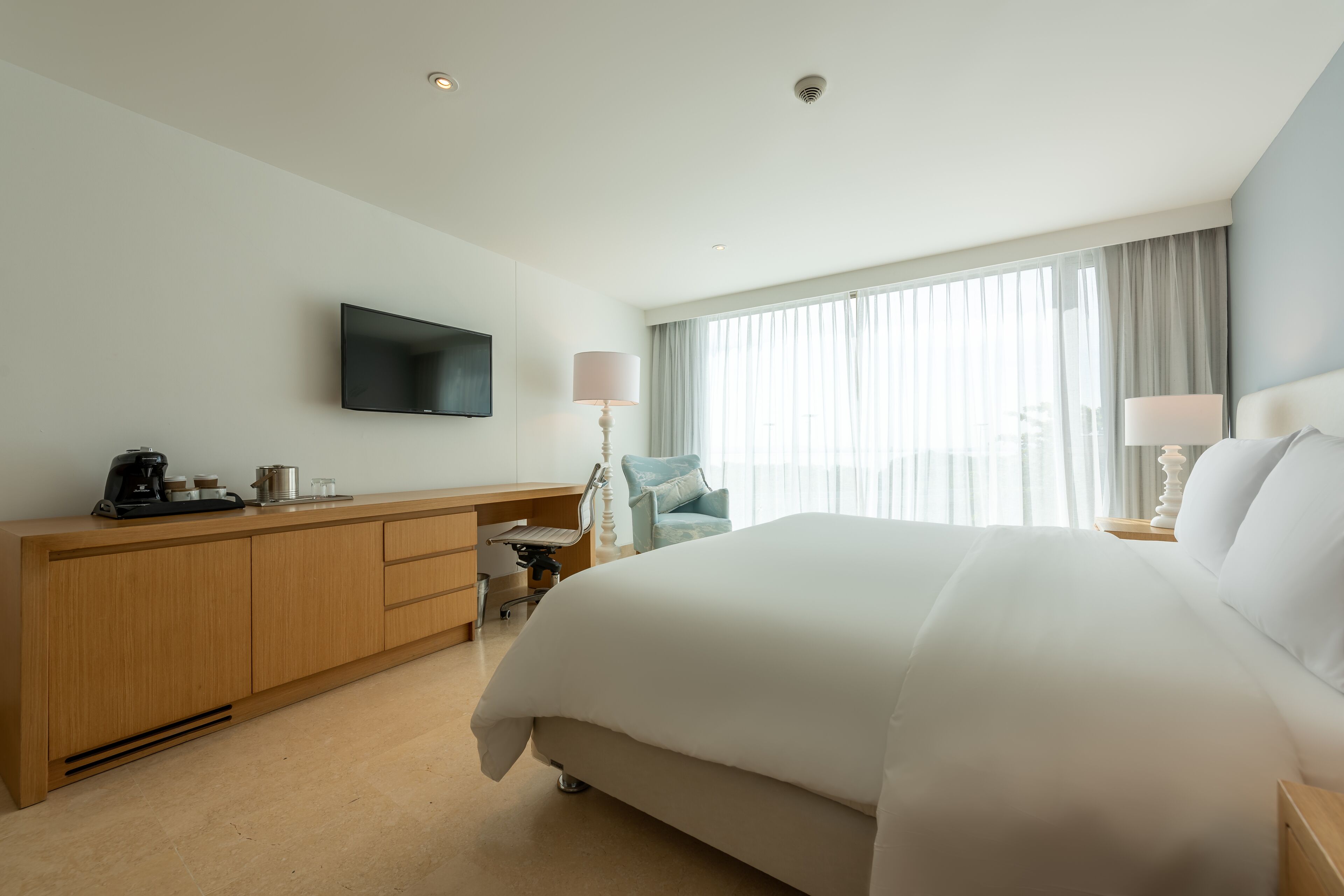 Habitación de hotel con una cama grande, un televisor de pantalla plana montado en la pared, un escritorio con silla y una ventana con cortinas.