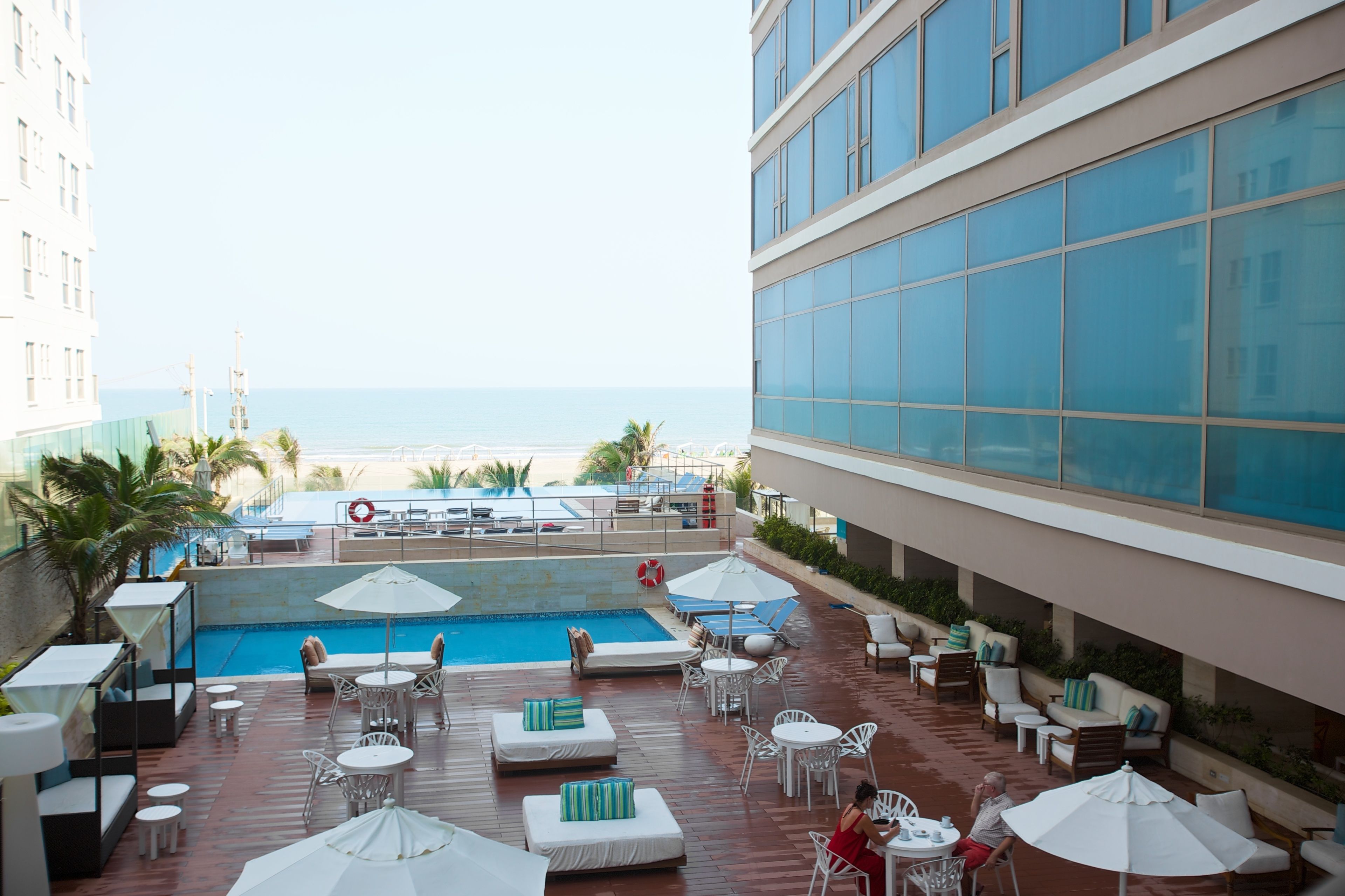 A rooftop pool area with lounge chairs, umbrellas, and a view of the beach.