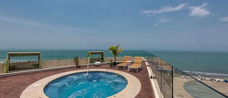 A rooftop pool with a view of the ocean, surrounded by lounge chairs and a glass balustrade.
