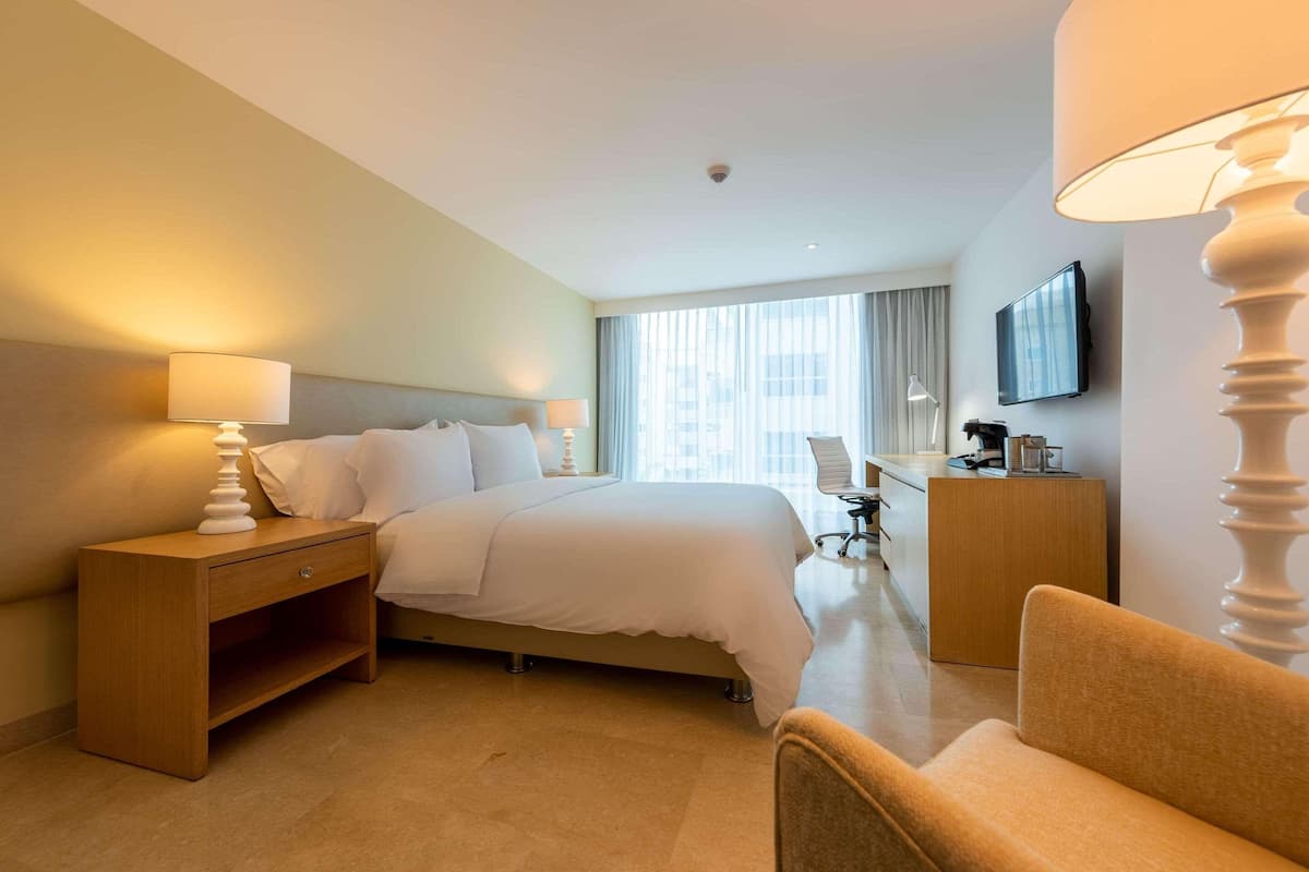 Une chambre d’hôtel comprenant un lit, une table de chevet, une lampe, une chaise, un bureau et un téléviseur.