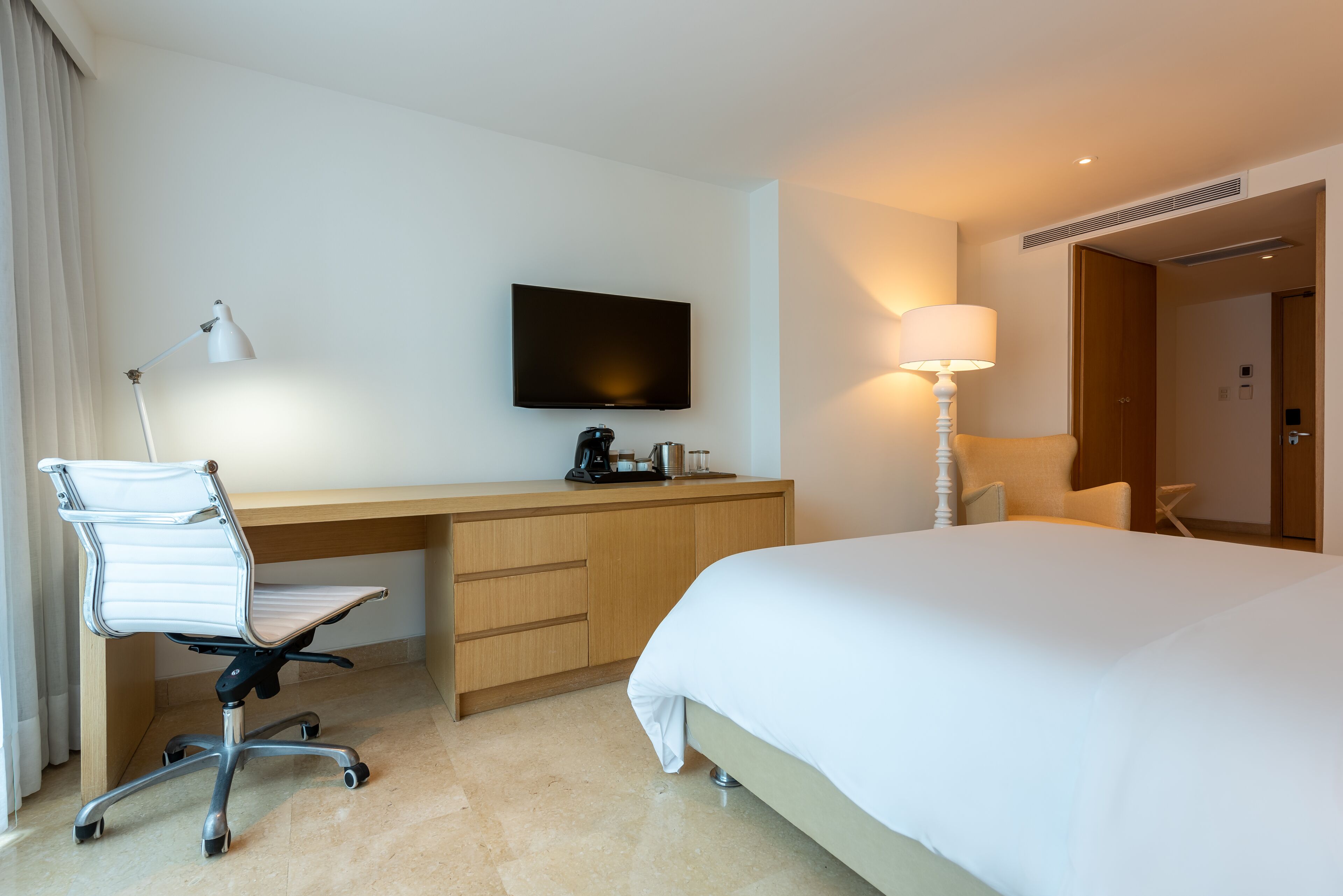 Een hotelkamer met een bed, een bureau met stoel, een televisie, een lamp en een koffiezetapparaat.