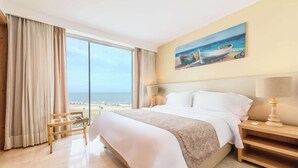 Una habitación de hotel con una cama grande, una mesita de noche, una lámpara y un cuadro de un barco en la pared.