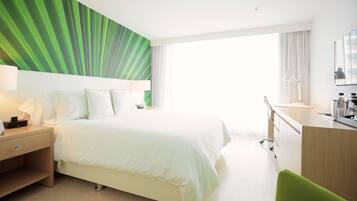 A hotel room with a large bed, a desk with a chair, a nightstand, and a green accent wall.