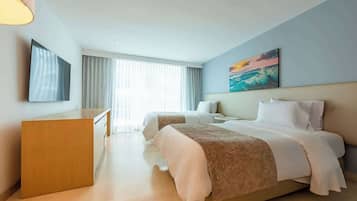 A hotel room with a desk, two beds, a painting, and a large window with curtains.