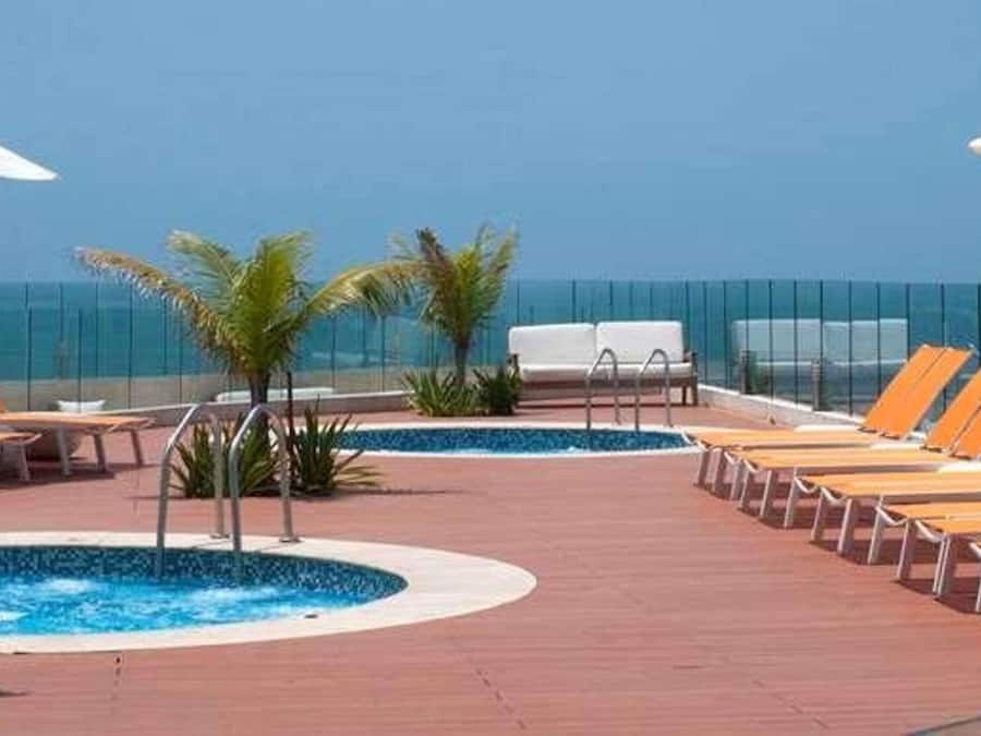 Zona junto a la piscina con sillones de descanso y sombrillas, una piscina pequeña y vista al océano.