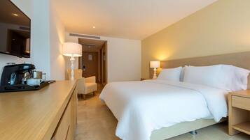 A hotel room with a bed, bedside tables, a desk with a coffee maker, a chair, and a TV mounted on the wall.
