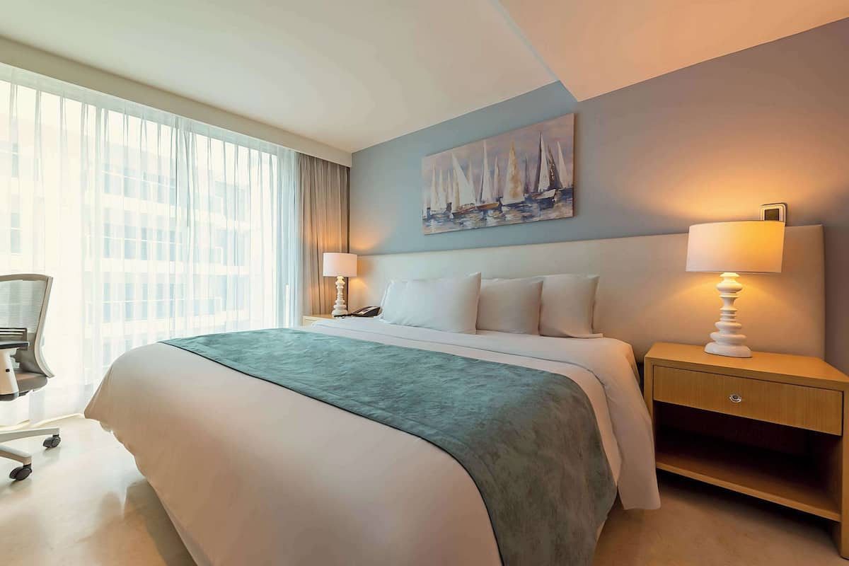 Une chambre d’hôtel avec un grand lit, un bureau, une chaise, une table de chevet avec une lampe et un tableau au mur.