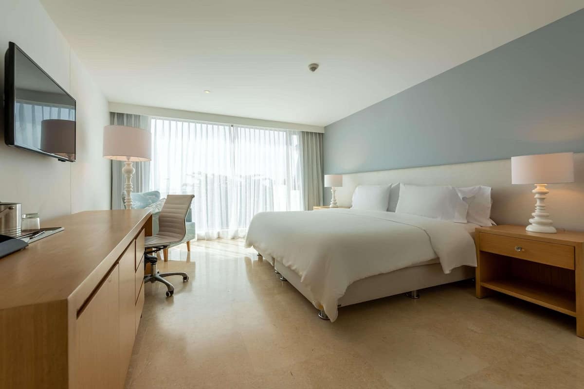 Une chambre d’hôtel avec un lit, un bureau, une chaise, une télévision et une fenêtre avec des rideaux.