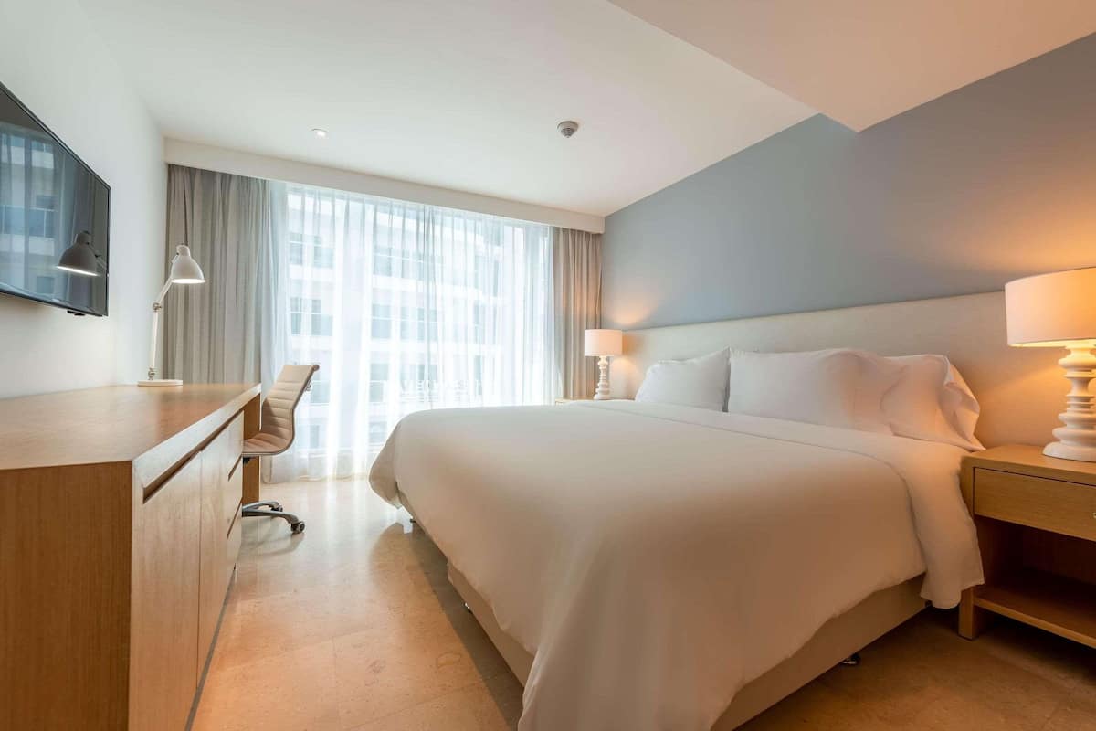Une chambre d’hôtel avec un grand lit, un bureau, une chaise et un téléviseur fixé au mur.