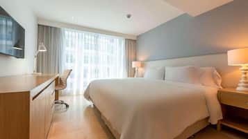 Habitación de hotel con una cama grande, un escritorio, una silla y un televisor en la pared.